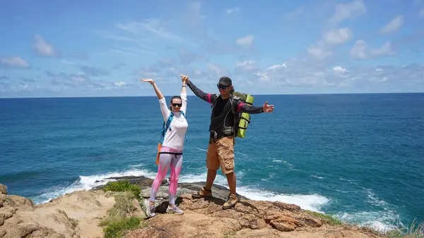 Genç bir çift okyanus manzarası sunan engebeli kayalık bir uçurumda yürüyüş yapıyor..