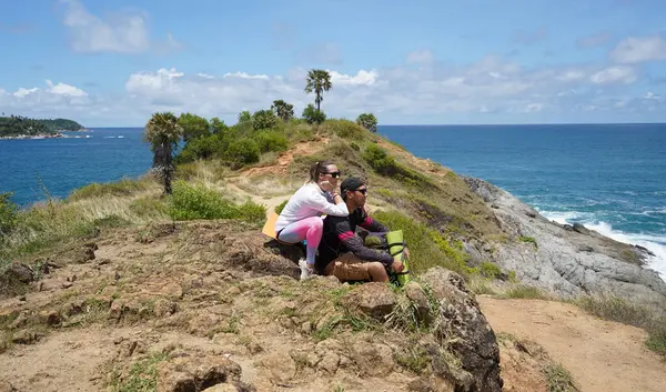 Genç bir çift okyanus manzarası sunan engebeli kayalık bir uçurumda yürüyüş yapıyor..