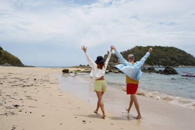 Genç bir çift kumsalda boş boş yürüyor, el ele tutuşuyor ve sıcak güneşin tadını çıkarıyor..