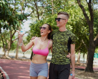 Bir adam ve bir kadın parkta birlikte koştuktan sonra şişelerden ferahlatıcı su içiyorlar..