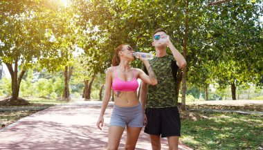 Bir adam ve bir kadın parkta birlikte koştuktan sonra şişelerden ferahlatıcı su içiyorlar..