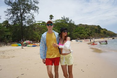 Genç bir çift kumsalda boş boş yürüyor, el ele tutuşuyor ve sıcak güneşin tadını çıkarıyor..