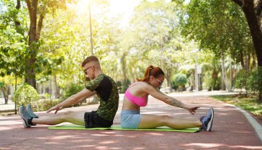 Renkli bir yoga minderinde bacaklarını açarken bir erkek bir kadına yardım ediyor..