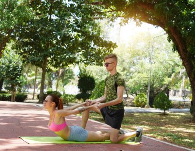 Renkli bir yoga minderinde bacaklarını açarken bir erkek bir kadına yardım ediyor..