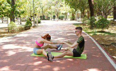 Renkli bir yoga minderinde bacaklarını açarken bir erkek bir kadına yardım ediyor..