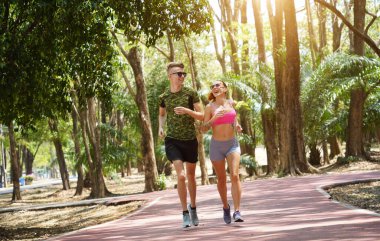 Bir adam ve bir kadın güzel bir parkta birlikte koşuyorlar, temiz havanın tadını çıkarıyorlar.