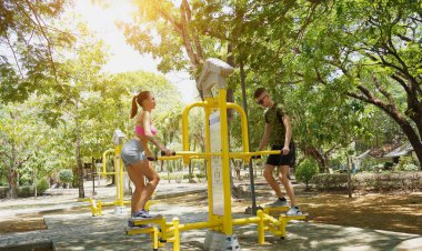 Bir adam ve kadın parkta bir makinede birlikte egzersiz yapıyorlar..