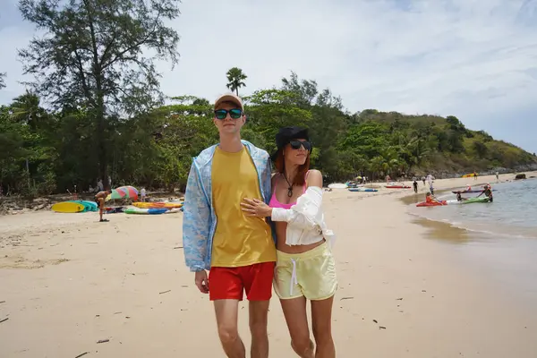 Genç bir çift kumsalda boş boş yürüyor, el ele tutuşuyor ve sıcak güneşin tadını çıkarıyor..