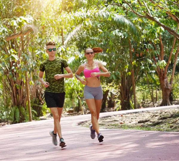 Bir adam ve bir kadın güzel bir parkta birlikte koşuyorlar, temiz havanın tadını çıkarıyorlar.
