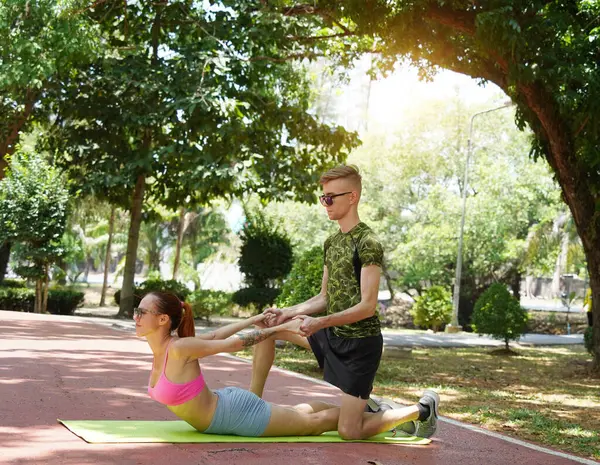 Renkli bir yoga minderinde bacaklarını açarken bir erkek bir kadına yardım ediyor..
