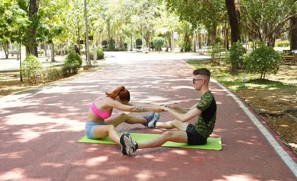 Renkli bir yoga minderinde bacaklarını açarken bir erkek bir kadına yardım ediyor..