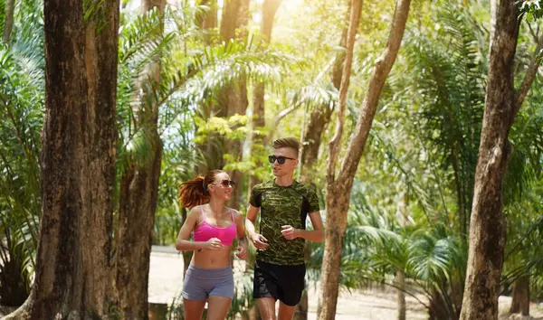 Bir adam ve bir kadın güzel bir parkta birlikte koşuyorlar, temiz havanın tadını çıkarıyorlar.