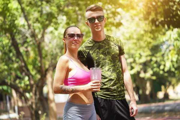 Bir adam ve bir kadın parkta birlikte koştuktan sonra şişelerden ferahlatıcı su içiyorlar..