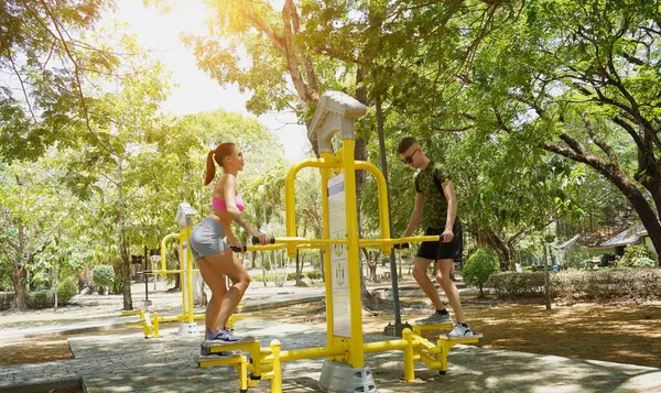 Bir adam ve kadın parkta bir makinede birlikte egzersiz yapıyorlar..