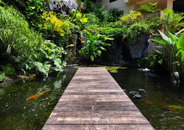 Büyüleyici bir ahşap köprü, sakin bir bahçede sakin bir gölet boyunca uzanır..