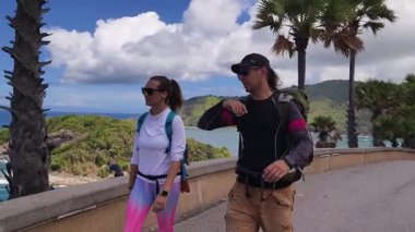 Bir erkek ve bir kadın, doğa güzelliği ve sükunetle çevrili bir yolda rahatça yürüyorlar..