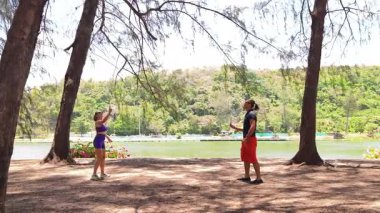 Bir adam ve genç bir kadın parkta badminton oynuyorlar..