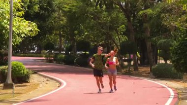 Bir adam ve bir kadın güzel bir parkta birlikte koşuyorlar, temiz havanın tadını çıkarıyorlar.