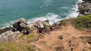 Genç bir çift okyanus manzarası sunan engebeli kayalık bir uçurumda yürüyüş yapıyor..