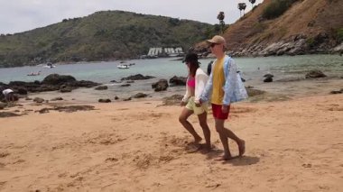 Genç bir çift kumsalda boş boş yürüyor, el ele tutuşuyor ve sıcak güneşin tadını çıkarıyor..