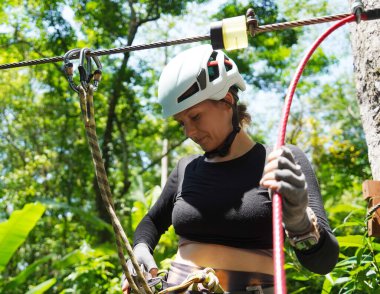 Kadın, etrafını saran kalın ormandan geçen bir halatla neşeli bir yolculuğun tadını çıkarıyor..