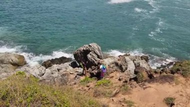 Genç bir çift okyanus manzarası sunan engebeli kayalık bir uçurumda yürüyüş yapıyor..