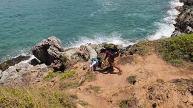 Genç bir çift okyanus manzarası sunan engebeli kayalık bir uçurumda yürüyüş yapıyor..