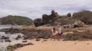 Genç bir çift kumsalda boş boş yürüyor, el ele tutuşuyor ve sıcak güneşin tadını çıkarıyor..