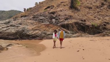 Genç bir çift kumsalda boş boş yürüyor, el ele tutuşuyor ve sıcak güneşin tadını çıkarıyor..