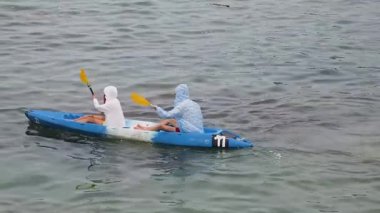 Genç çift, açık mavi bir kanoyla birlikte sarı raketlerle mutlu bir şekilde yol alıyorlar..