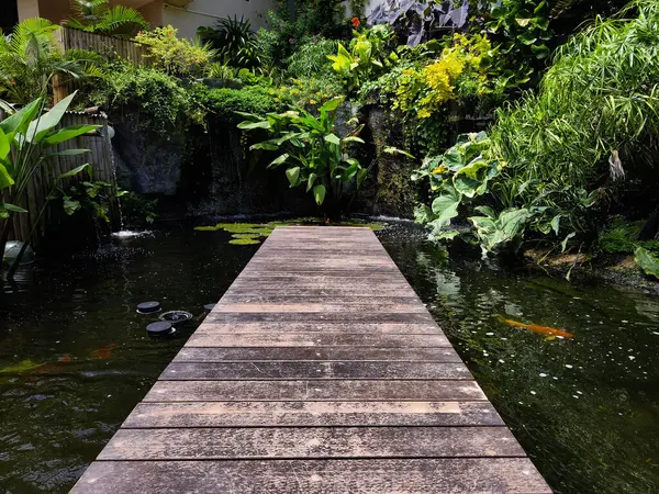 Büyüleyici bir ahşap köprü, sakin bir bahçede sakin bir gölet boyunca uzanır..