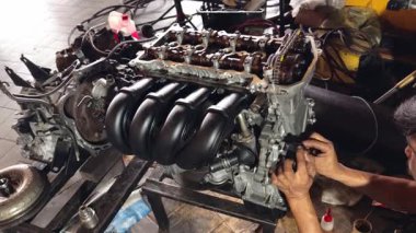 Servis elemanı özenle garajın içindeki bir araba motoru üzerinde çalışıyor..