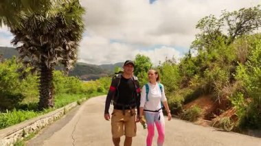 Bir erkek ve bir kadın, doğa güzelliği ve sükunetle çevrili bir yolda rahatça yürüyorlar..