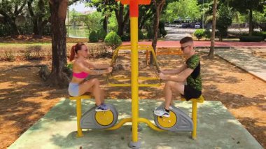Bir adam ve kadın parkta bir makinede birlikte egzersiz yapıyorlar..