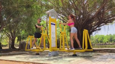 Bir adam ve kadın parkta bir makinede birlikte egzersiz yapıyorlar..