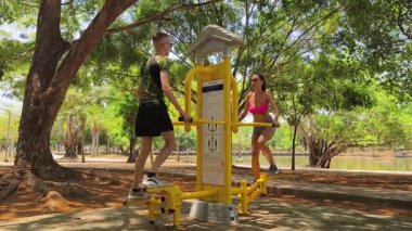 Bir adam ve kadın parkta bir makinede birlikte egzersiz yapıyorlar..