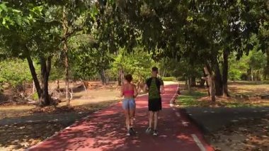 Bir adam ve bir kadın güzel bir parkta birlikte koşuyorlar, temiz havanın tadını çıkarıyorlar.