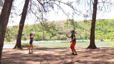 Bir adam ve genç bir kadın parkta badminton oynuyorlar..