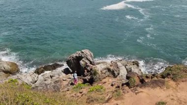 Genç bir çift okyanus manzarası sunan engebeli kayalık bir uçurumda yürüyüş yapıyor..
