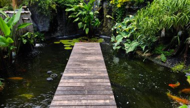 Büyüleyici bir ahşap köprü, sakin bir bahçede sakin bir gölet boyunca uzanır..