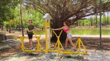 Bir adam ve kadın parkta bir makinede birlikte egzersiz yapıyorlar..