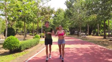 Bir adam ve bir kadın güzel bir parkta birlikte koşuyorlar, temiz havanın tadını çıkarıyorlar.