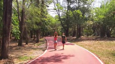 Bir adam ve bir kadın güzel bir parkta birlikte koşuyorlar, temiz havanın tadını çıkarıyorlar.