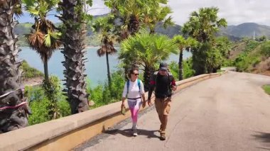 Bir erkek ve bir kadın, doğa güzelliği ve sükunetle çevrili bir yolda rahatça yürüyorlar..