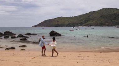 Genç bir çift kumsalda boş boş yürüyor, el ele tutuşuyor ve sıcak güneşin tadını çıkarıyor..