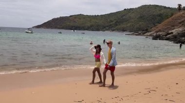 Genç bir çift kumsalda boş boş yürüyor, el ele tutuşuyor ve sıcak güneşin tadını çıkarıyor..