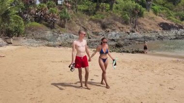 Genç bir çift kumsalda boş boş yürüyor, el ele tutuşuyor ve sıcak güneşin tadını çıkarıyor..