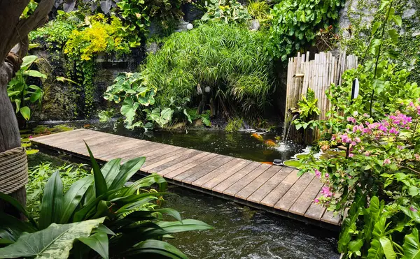 Büyüleyici bir ahşap köprü, sakin bir bahçede sakin bir gölet boyunca uzanır..