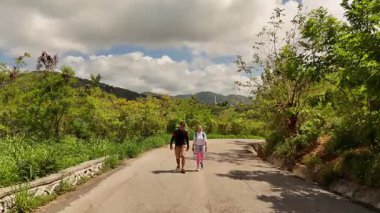 Bir erkek ve bir kadın, doğa güzelliği ve sükunetle çevrili bir yolda rahatça yürüyorlar..