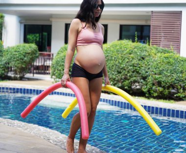 Bilardo oynamak üzere olan hamile genç kadın köpüklü makarnayla havuzda egzersiz yapacak..